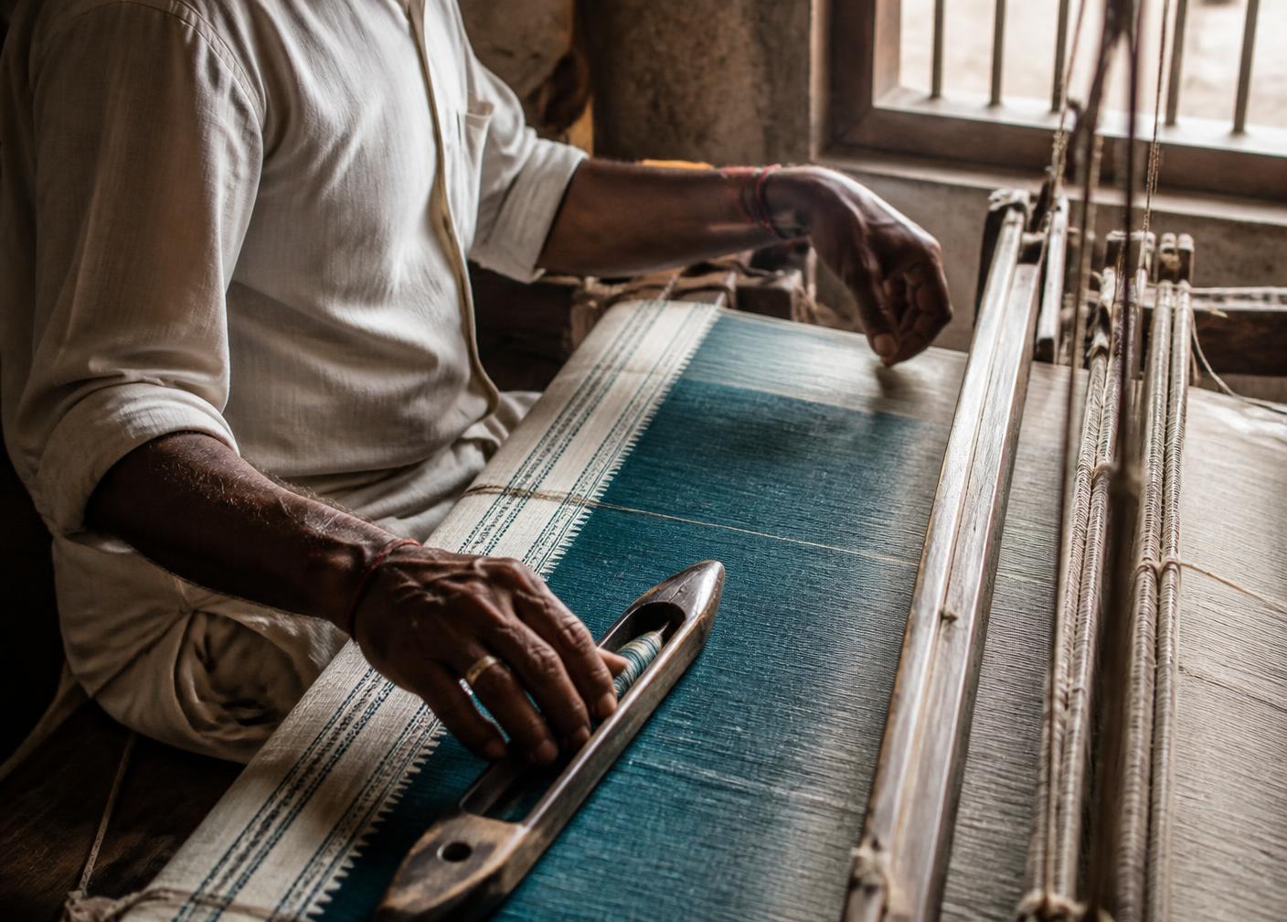 Indian weaver working teal and ivory cloth on a traditional wooden handloom
